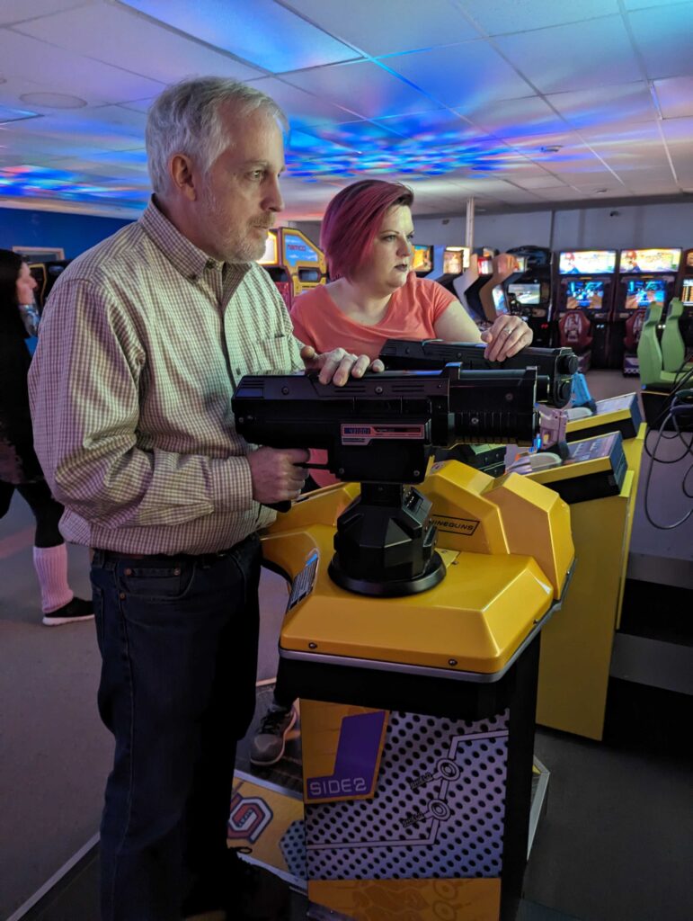 A man and a woman look to the right of the camera deeply engaged in an arcade shooter off-screen